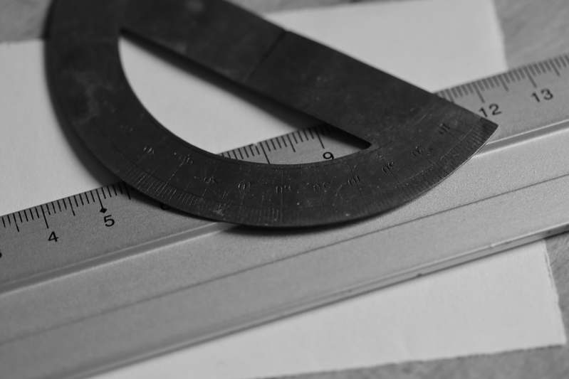 Stack of vintage and modern protractors — brass, plastic, and digital — on a clean white background